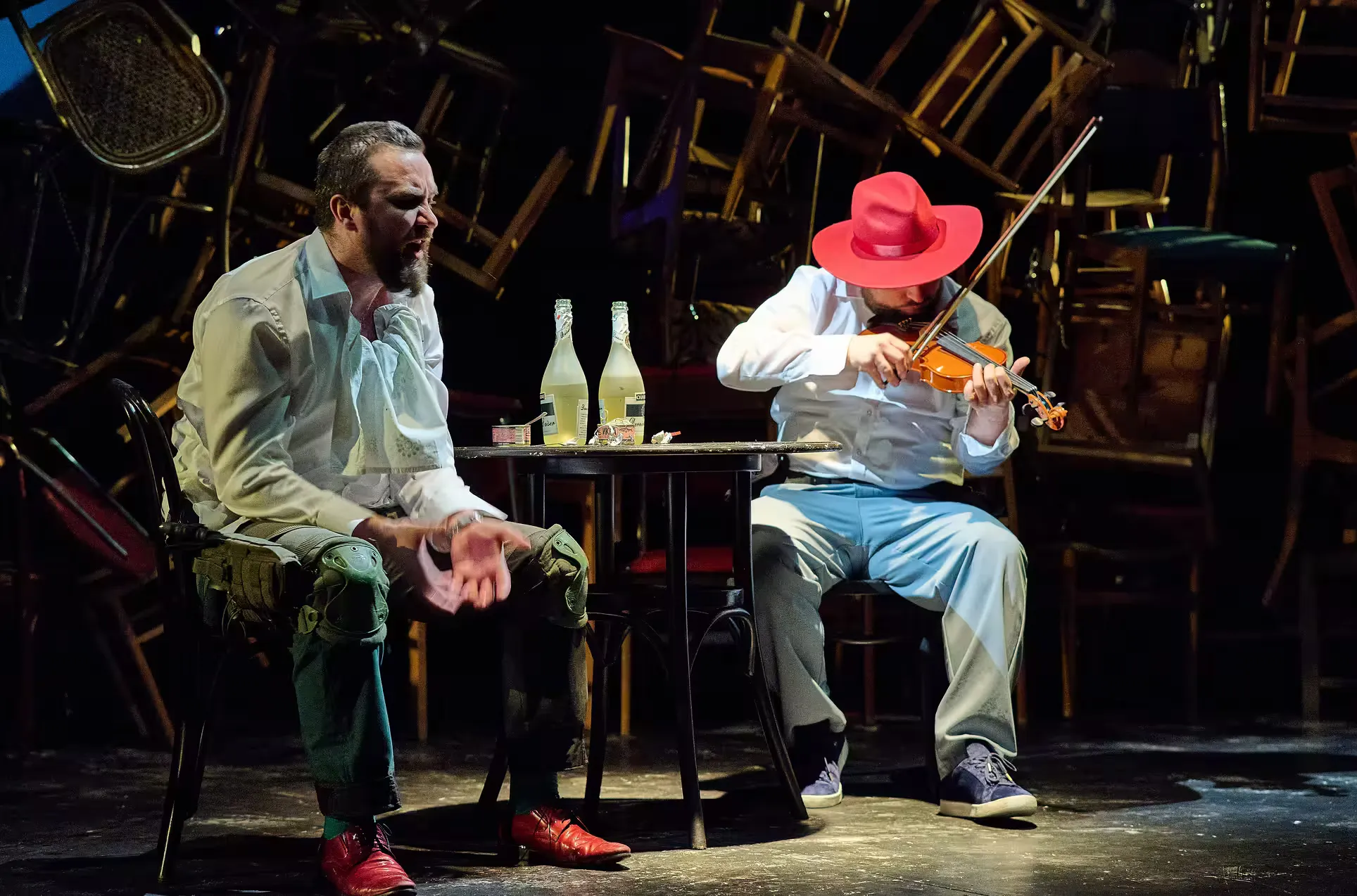 Medium shot of two acros sitting. One is playing a violin