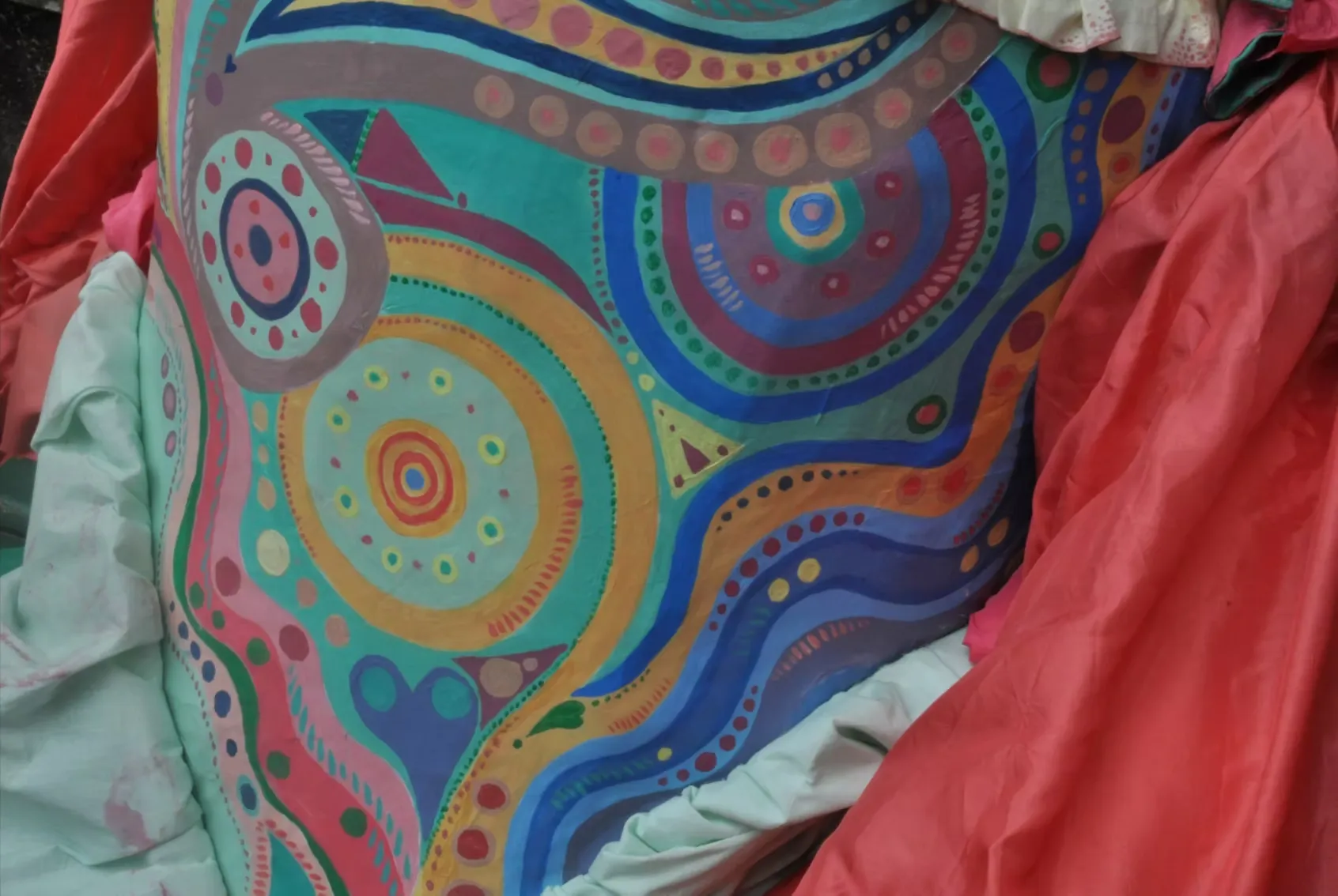 Close-up of a large puppet body painted with swirling concentric circles, dots, and wave patterns in turquoise, blue, orange, and pink. Vivid folk-art patterning that fills the entire surface.