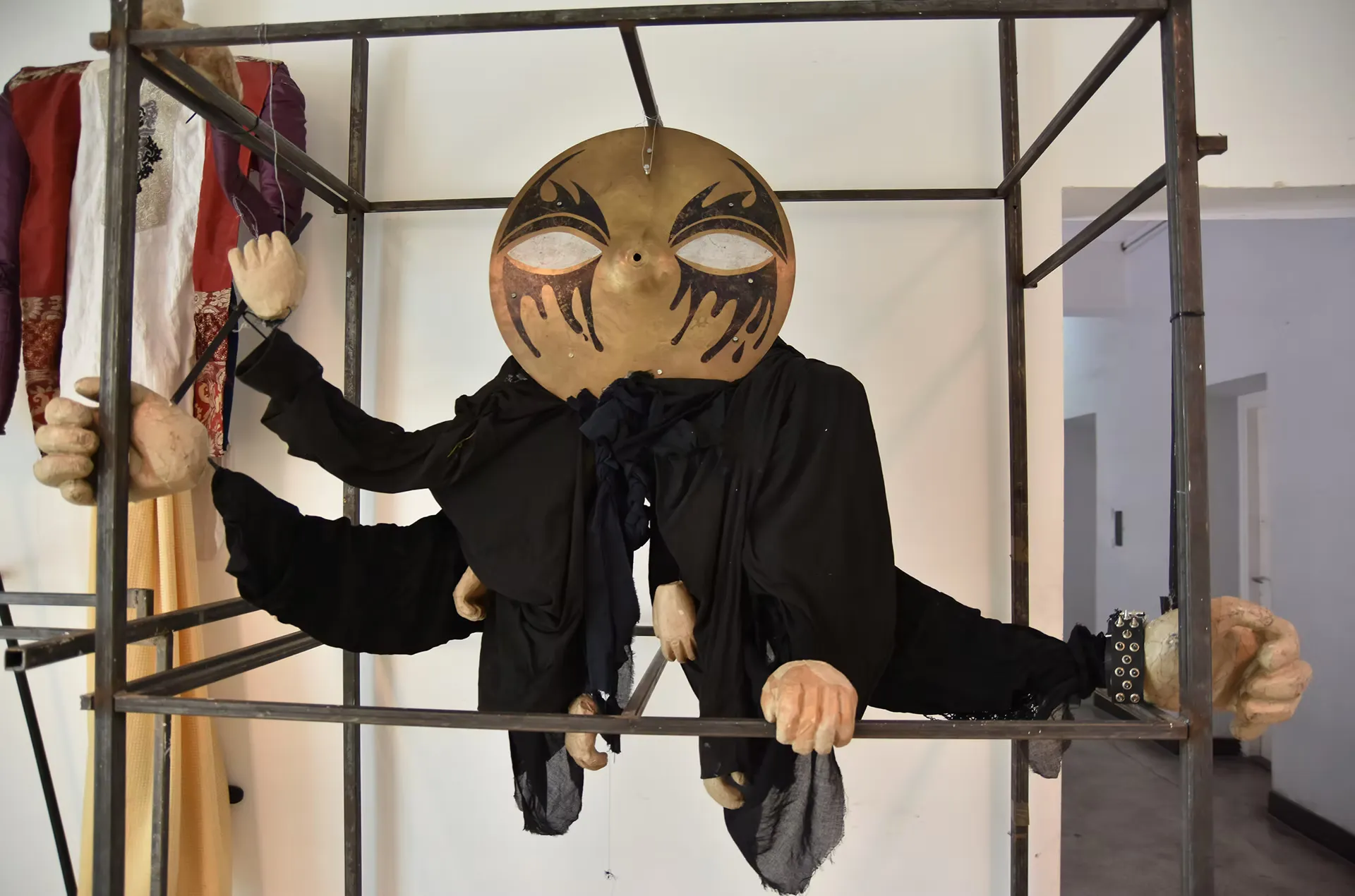 The large golden-masked puppet displayed on metal scaffolding in an exhibition or rehearsal space, with other costumes visible behind it. Scale and craftsmanship on full display.